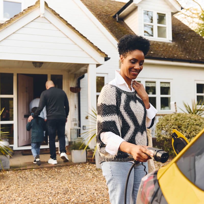 Woman connecting an electric vehicle charger to a car outside a home, showcasing the convenience of EV charging installations.