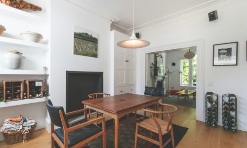 Modern dining area featuring a wooden table and chairs, with decorative shelves displaying pottery and a landscape painting on the wall, showcasing a bright, inviting interior space.