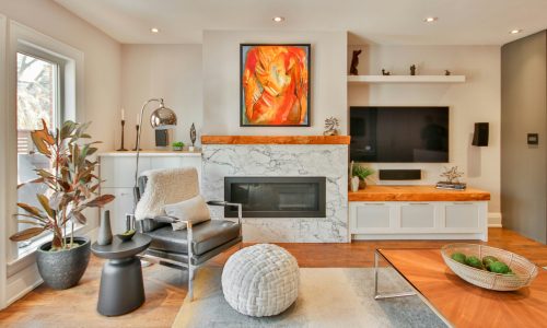 Modern living room featuring a stylish armchair, decorative plants, a marble fireplace, and an abstract painting, illustrating a comfortable and contemporary home environment.